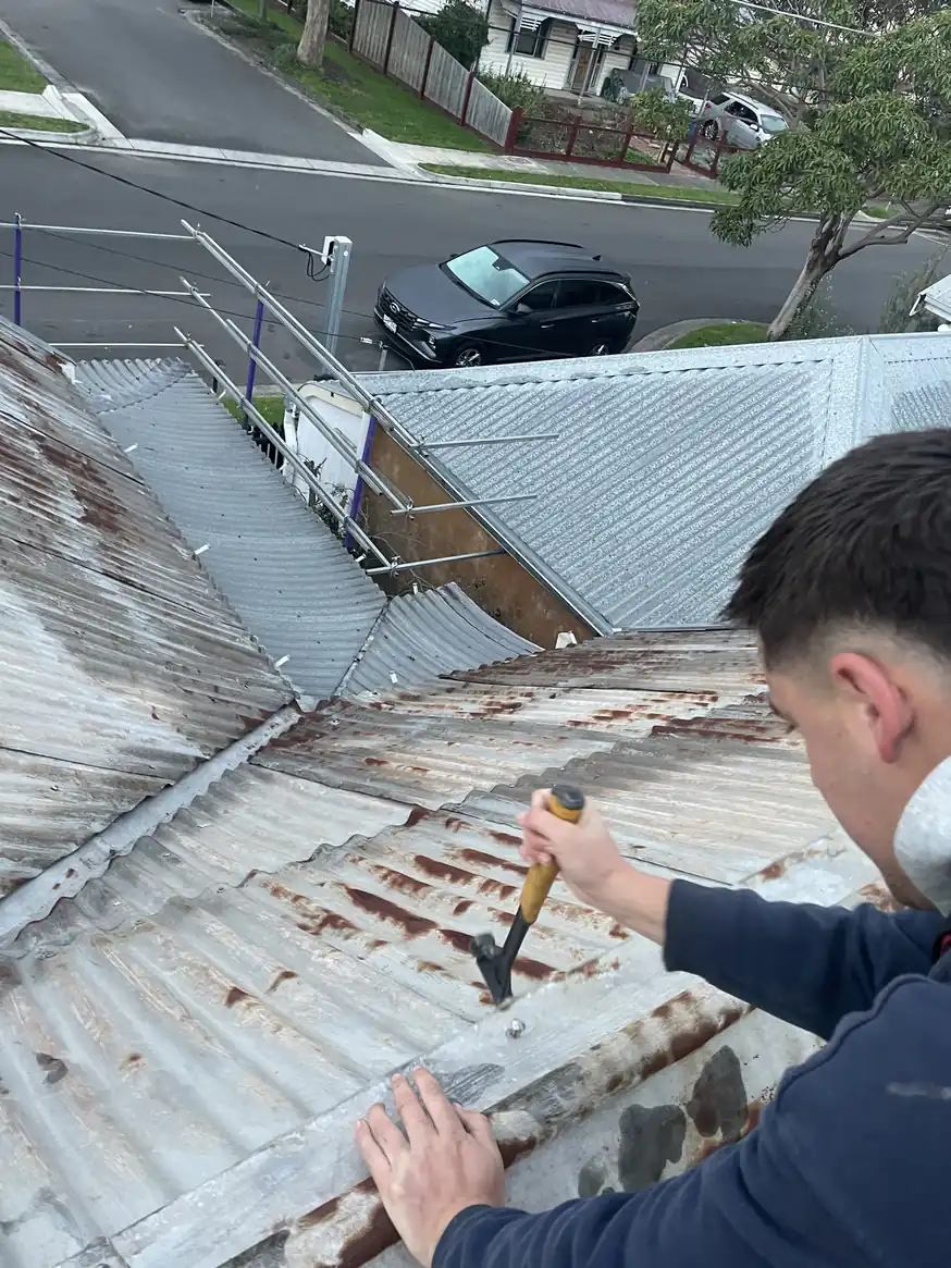 A Barnes Family Roof Plumbing apprentice repairing an old corrugated metal roof