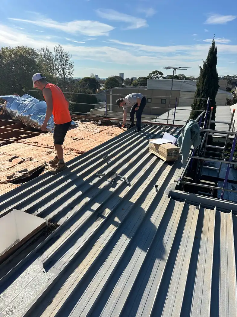 Barnes Family Roof Plumbing crew laying new metal roof sheets over a stripped roof in Geelong